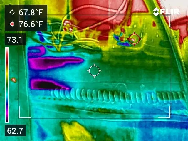 Rainbow-palette thermal image of the top of a wall beside an exhaust duct with a cold band in purple and blue