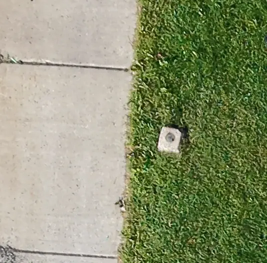 Close-up from a drone orthomosaic showing an existing survey monument set in grass beside a sidewalk